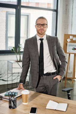 Gözlüklü, gri takım elbiseli, el ele tutuşup kameraya bakan kendine güvenen bir iş adamı.