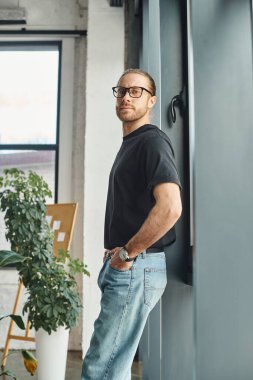 Siyah tişörtlü başarılı iş adamı elleri ceplerinde kameraya bakıyor.