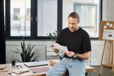 thoughtful manager in casual attire sitting on work desk and looking at documents in office clipart