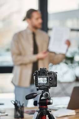 Bulanık iş adamının yanındaki modern dijital kameranın seçici odak noktası ofiste video blogu kaydediyor