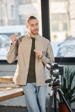 Modern ofisteki video blogu sırasında dijital kamera yanında bitcoin gösteren yaratıcı iş adamı