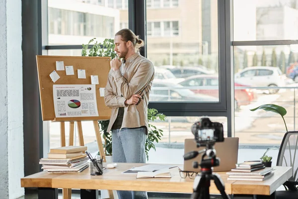 stock image thoughtful businessman looking at flip charts with infographics near digital camera in office
