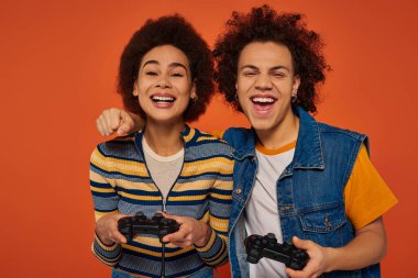 Neşeli genç Afrikalı Amerikalı erkek ve kız kardeş joysticklerle video oyunu oynuyorlar, aile kavramı.
