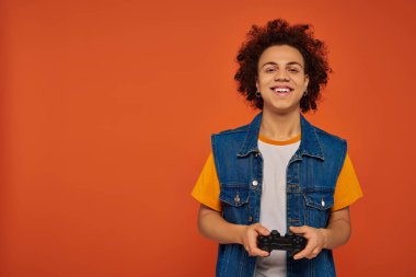 Genç, yakışıklı Afrikalı Amerikalı adam duygusal olarak turuncu arka planda joystick ile video oyunu oynuyor.