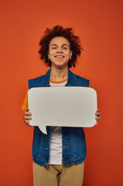 jolly african american male model in casual attire posing with speech bubble on orange backdrop clipart