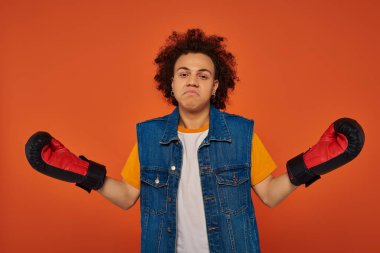 confused sporty african american male model posing lively in boxing gloves on orange background clipart