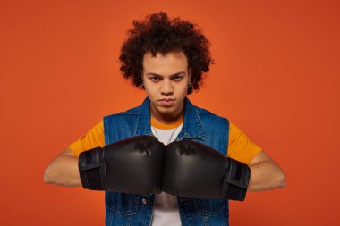 good looking sporty african american man posing actively in boxing gloves on orange background clipart