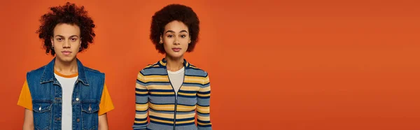 stock image emotional african american siblings in vibrant outfits posing together on orange background, banner