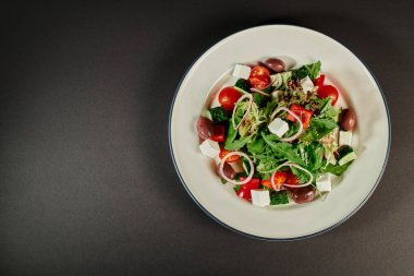 Gri arka planda taze yapılmış Yunan salatası ve sağlıklı beslenme içeren tabağın en üst görüntüsü.