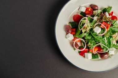 Gri arka planda taze ve lezzetli Yunan salatasıyla tabağın üst görüntüsü, sağlıklı beslenme