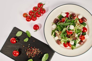 Çeri domates ve fesleğen yapraklarının yanında geleneksel Yunan salatasıyla tabağın en üst görüntüsü