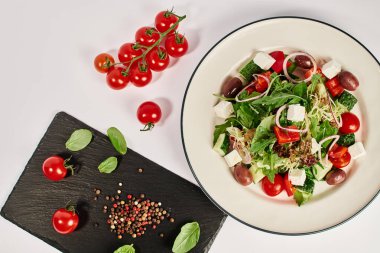 top view photo of plate with traditional Greek salad near cherry tomatoes and basil leaves clipart