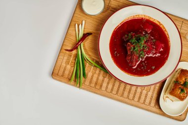 Sarımsaklı çöreklerin yanında taze dereotu ve kesme tahtasında ekşi kremayla geleneksel Ukrayna borsch 'u.