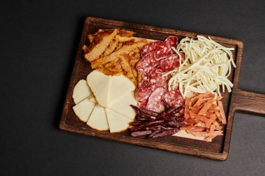 Gurme peynir seçimi, kurutulmuş sığır eti ve siyah salam dilimli şarküteri panosunun üst görüntüsü.