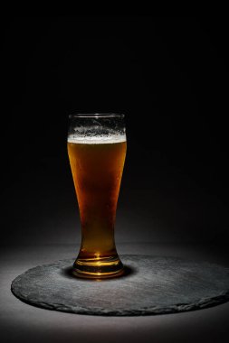 Bir bardak bira ya da köpüklü bira. Siyah arka plandaki bardak altlığında soğutulmuş cam.