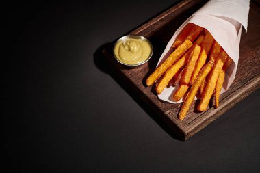 Tahta kesme tahtasına batırılmış sosun yanında, kağıt koninin içinde nefis ev yapımı patates kızartması.
