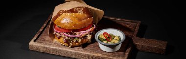 Tahta tepside siyah pankartta susamlı hamburger, biftek ve turşu.