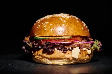 Jambonlu sulu hamburger, kırmızı soğan, erimiş peynir ve siyah arkaplanda susamlı çörek.
