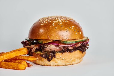 Sığır etli, kırmızı soğanlı, domatesli ve susamlı hamburgerin yanında patates kızartması.