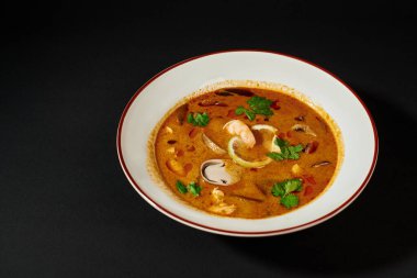 spicy Tom yum soup with coconut milk, shrimp, lemongrass and cilantro on black background clipart