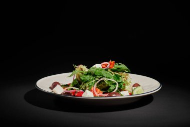 Sağlıklı beslenme, feta peynirli Yunan salatası, kırmızı soğan, siyah arkaplanda roka yaprakları.