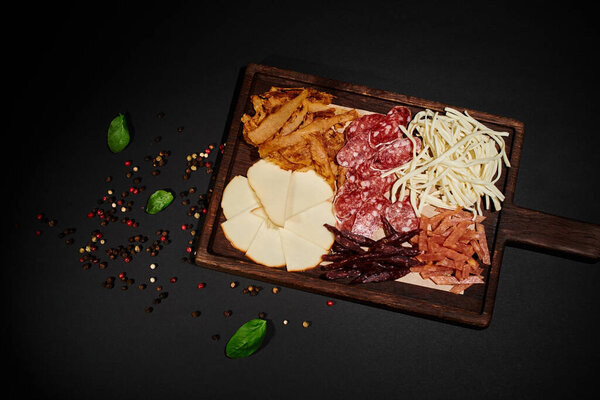 top view of party food board with gourmet cheese selection, dried beef and salami slices on black
