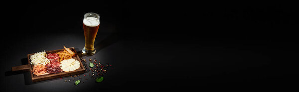 glass of craft lager near charcuterie board with gourmet cheese, dried beef and salami, banner