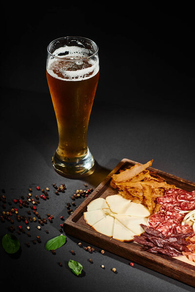 glass of craft beer near charcuterie board with gourmet cheese, dried beef and salami on board