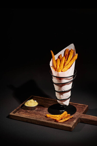 вкусный хрустящий картофель фри внутри бумажного конуса рядом с макающим соусом на деревянной доске