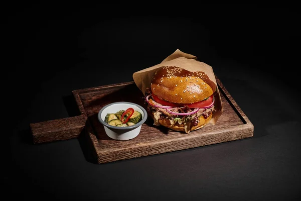 stock image delicious hamburger with sesame bun, beef and pickles as side dish on wooden tray on black