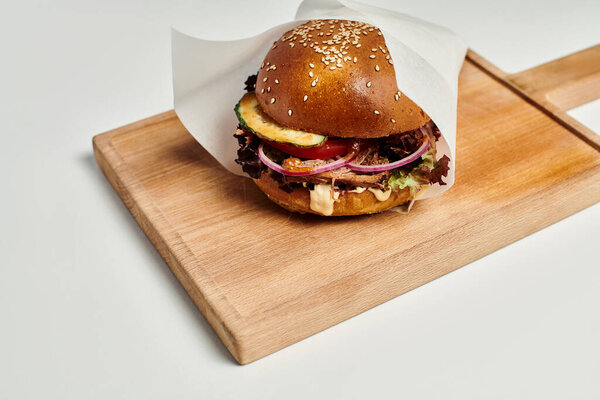 juicy hamburger with grilled beef, red onion, cheese melt and sesame bun on wooden cutting board