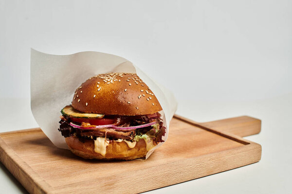 tasty hamburger with grilled beef, red onion, cheese melt and sesame bun on wooden cutting board