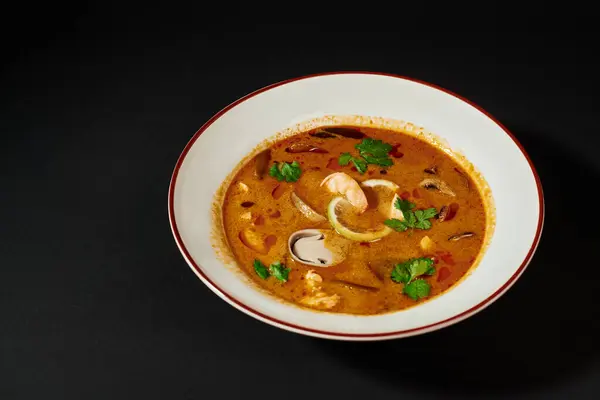 stock image spicy Tom yum soup with coconut milk, shrimp, lemongrass and cilantro on black background