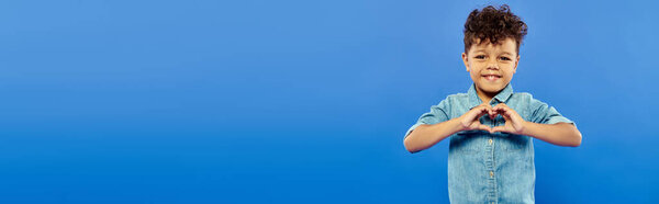 счастливый африканский американский дошкольник в стильной джинсовой одежде, показывающий сердце с руками, баннер