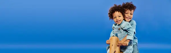 stock image happy african american kids in stylish denim clothes sitting on rocking horse on blue, banner