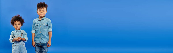 счастливый африканский американский дошкольник в джинсовой одежде, стоящий рядом с младшим братом, баннер