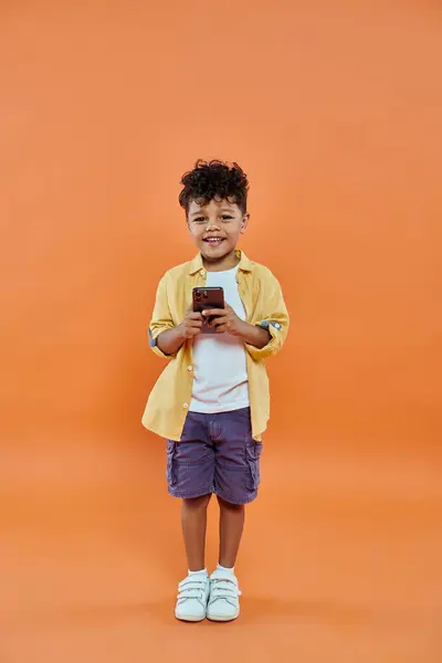 Stock image happy african american preschooler boy in casual attire using smartphone on orange background