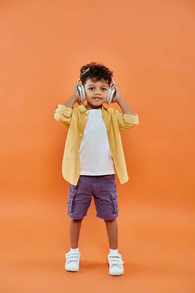 stock image cheerful and curly african american boy listening music in wireless headphones on orange background