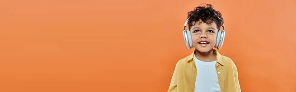 快乐而卷曲的非洲裔美国男孩 在橙色横幅上的无线耳机里听音乐 — 图库照片