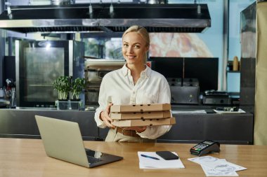 Dijital cihazların yanında pizza kutularıyla gülümseyen sarışın kadın ve kafede ödeme terminali.