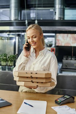 Pizza kutularıyla neşeli kafe müdürü ödeme terminalinin yanında cep telefonuyla konuşuyor.