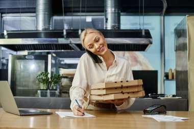 Pizza kutularıyla mutlu sarışın kadın akıllı telefonla konuşuyor ve kafede sipariş yazıyor.