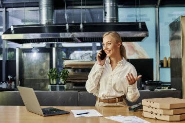 Pizza kutularının yanında akıllı telefondan konuşan bir kafe yöneticisi ve dizüstü bilgisayarlı ödeme terminali.
