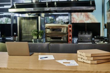 Modern kafe ortamındaki ahşap tezgahta pizza kutularının ve menü kartlarının yanında dizüstü bilgisayar, samimi bir atmosfer.
