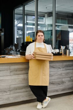 Down sendromlu genç bayan çalışan modern kafede pizza kutularıyla ayakta duruyor.