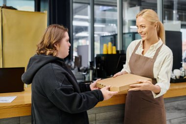 Neşeli bayan yönetici modern kafede Down sendromu olan genç bir kadına pizza kutusu veriyor.