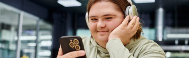 Ruhsal bozukluğu olan mutlu bir kadın kulaklıkla müzik dinliyor ve kafeteryada akıllı telefon tutuyor.