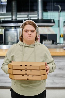Modern kafede pizza kutuları taşıyan, kablosuz kulaklıklı genç bir kadın.