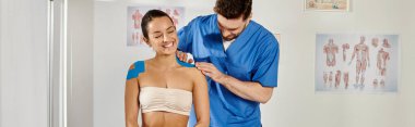 Yakışıklı doktoru vücuduna Kinesio bantları yapıştırırken neşeli ve çekici bir kadın oturuyor.