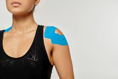 Omuzlarında ve boynunda kineziyolojik bantlarla spor kıyafeti giymiş genç bir kadın.